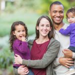 Mom and dad smile while holding their 2 daughters outside before going to their family dentist in Denver, CO