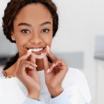 Pretty brown eyed girl holding a clear aligner in front of her smile.