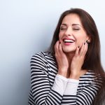 Brunette woman in a striped shirt smiles while touching the sides of her face