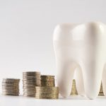 A white tooth next to several stacks of coins